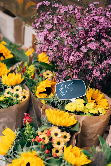 A vibrant display of freshly arranged floral bouquets at an outdoor flower market, featuring bright yellow sunflowers, small white daisies with yellow centers, and red and pink blooms, all wrapped in